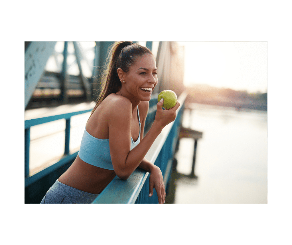 Athletic woman eating apple on bridge and smiling