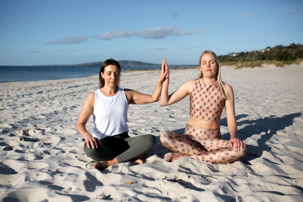 2 women doing yoga on beach.