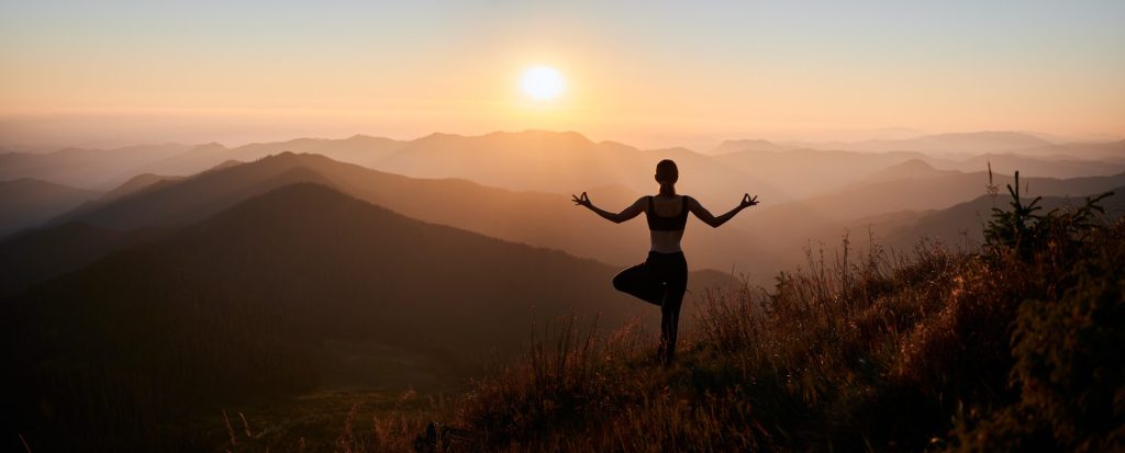 Woman on mountain practicing her yoga and balance in front of a beautiful view.