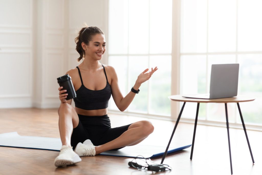 Woman taking an online wellness coaching class from her laptop at home while sitting on a mat.