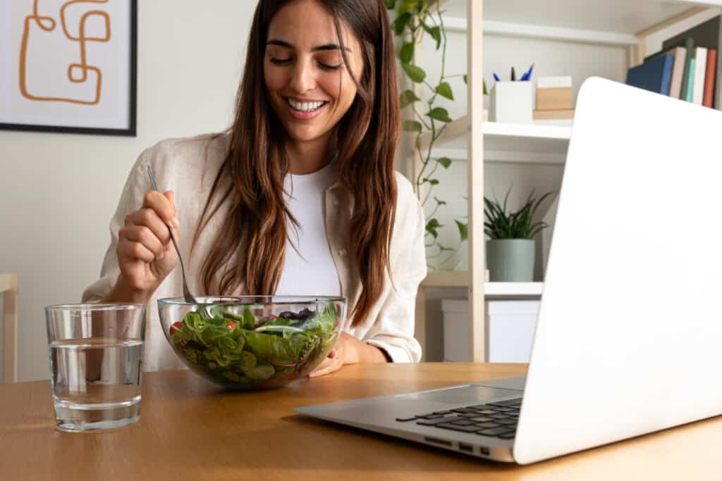 Woman eating a healthy salad while reading about how to empower yourself after a breakup on laptop.