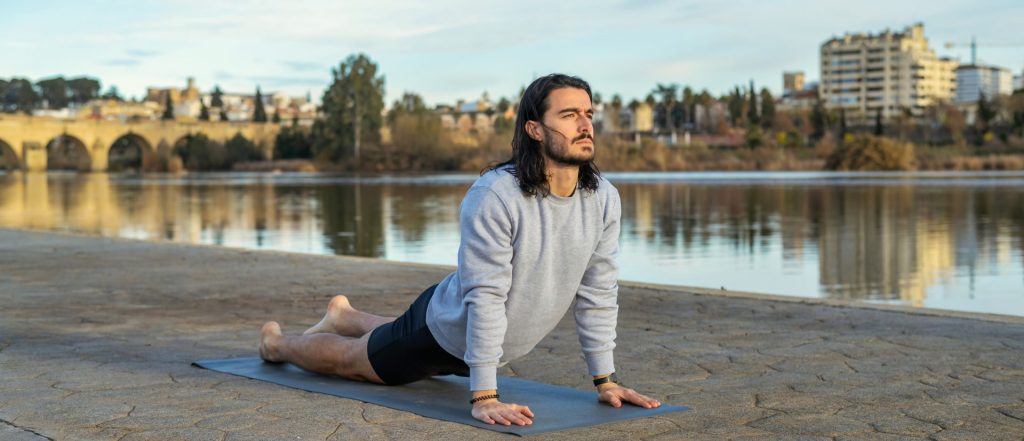 Man on a mat doing a pose next to water for yoga and weight loss.