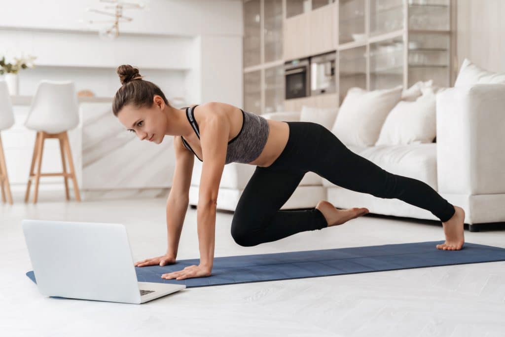 Woman doing workout at home with laptop next to her.